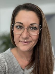 Nahaufnahme einer lächelnden Frau mit Brille und Piercings